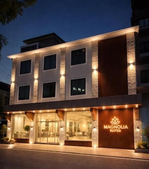 Un hotel moderno con fachada de piedra, amplias ventanas y una entrada visible con un cartel que dice 'Magnolia Suites'.