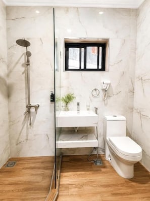A bathroom with a glass-enclosed shower, a white sink, a toilet, and a small window. - Magnolia Suites B&B (Dar es Salaam)