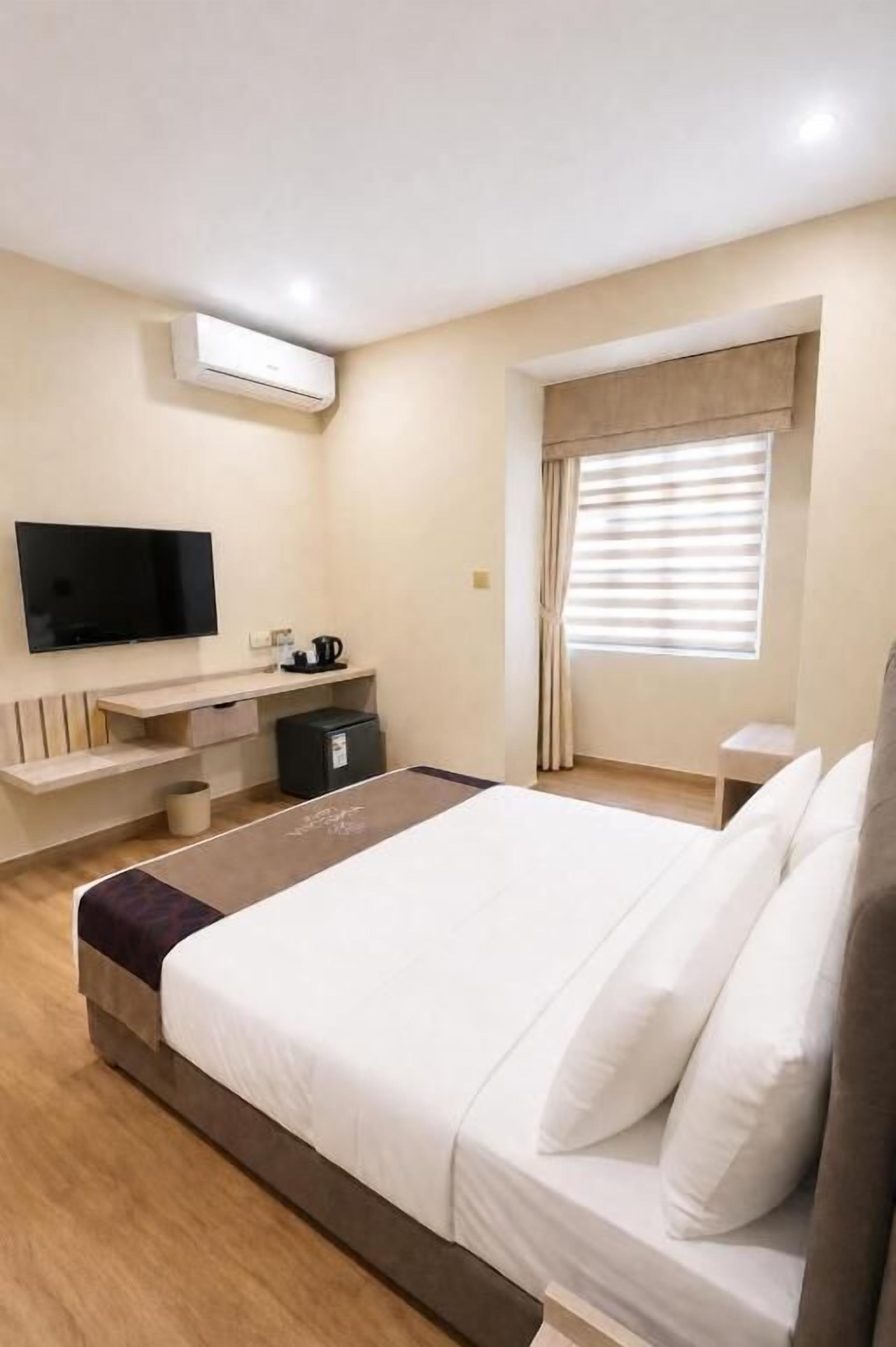 Een hotelkamer met een bed, een televisie, een bureau en een raam met zonwering.