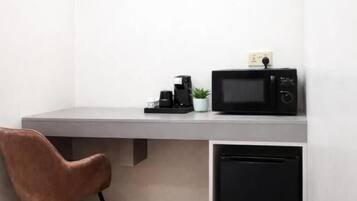 Una habitación compacta con un escritorio blanco, un microondas negro, un pequeño electrodoméstico negro y una silla marrón.