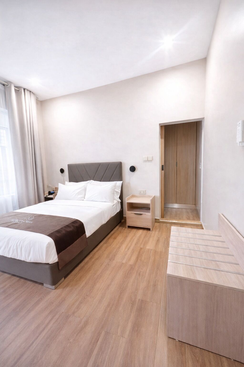 A modern hotel room with a bed, bedside table, and a wooden wardrobe.