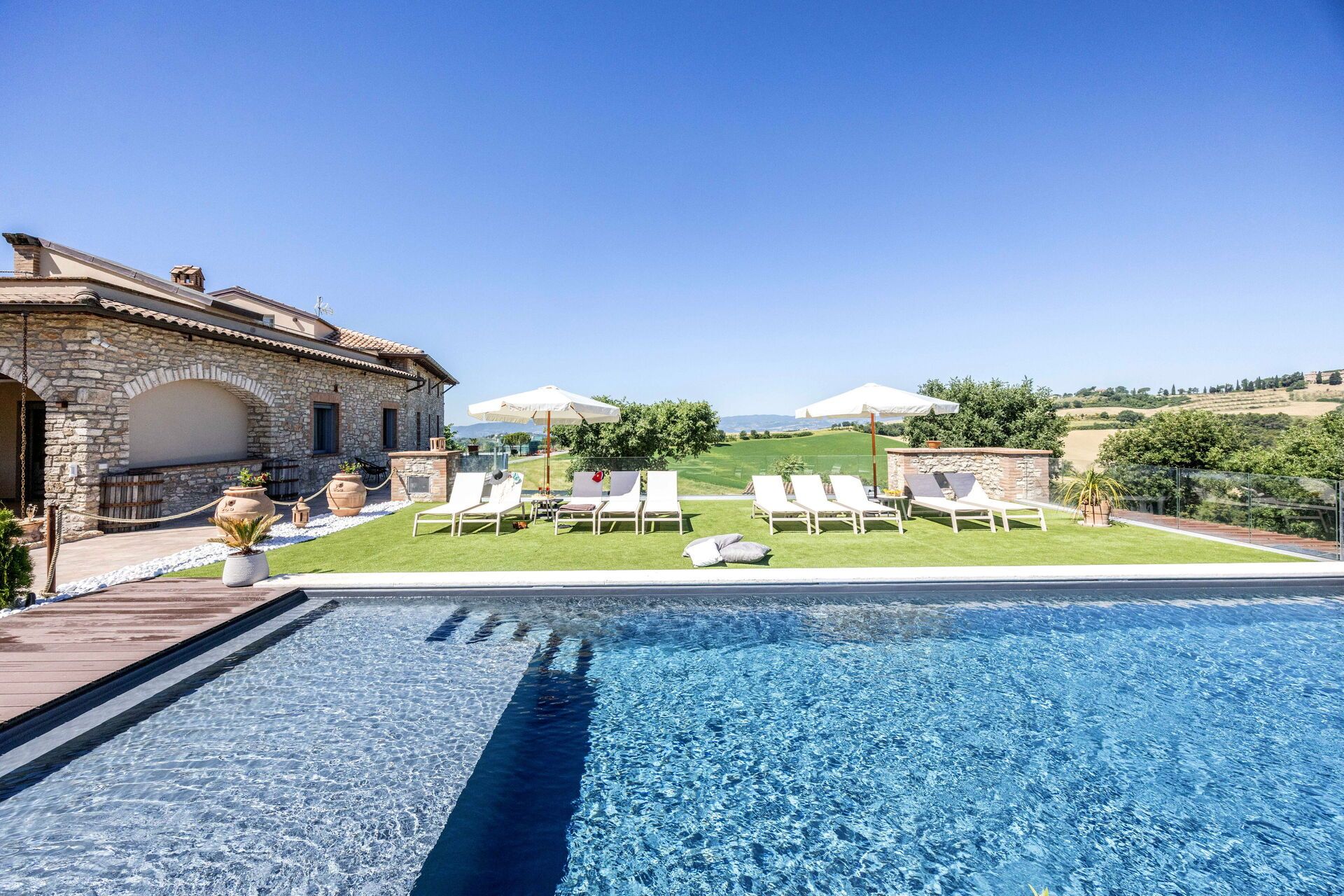 A swimming pool with lounge chairs and umbrellas, a stone building, and a view of the countryside.