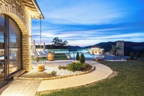 A modern outdoor pool area with lounge chairs and umbrellas, surrounded by a stone wall and a view of mountains. - Villa in Canale with 5 bedrooms sleeps 14 (Canale)