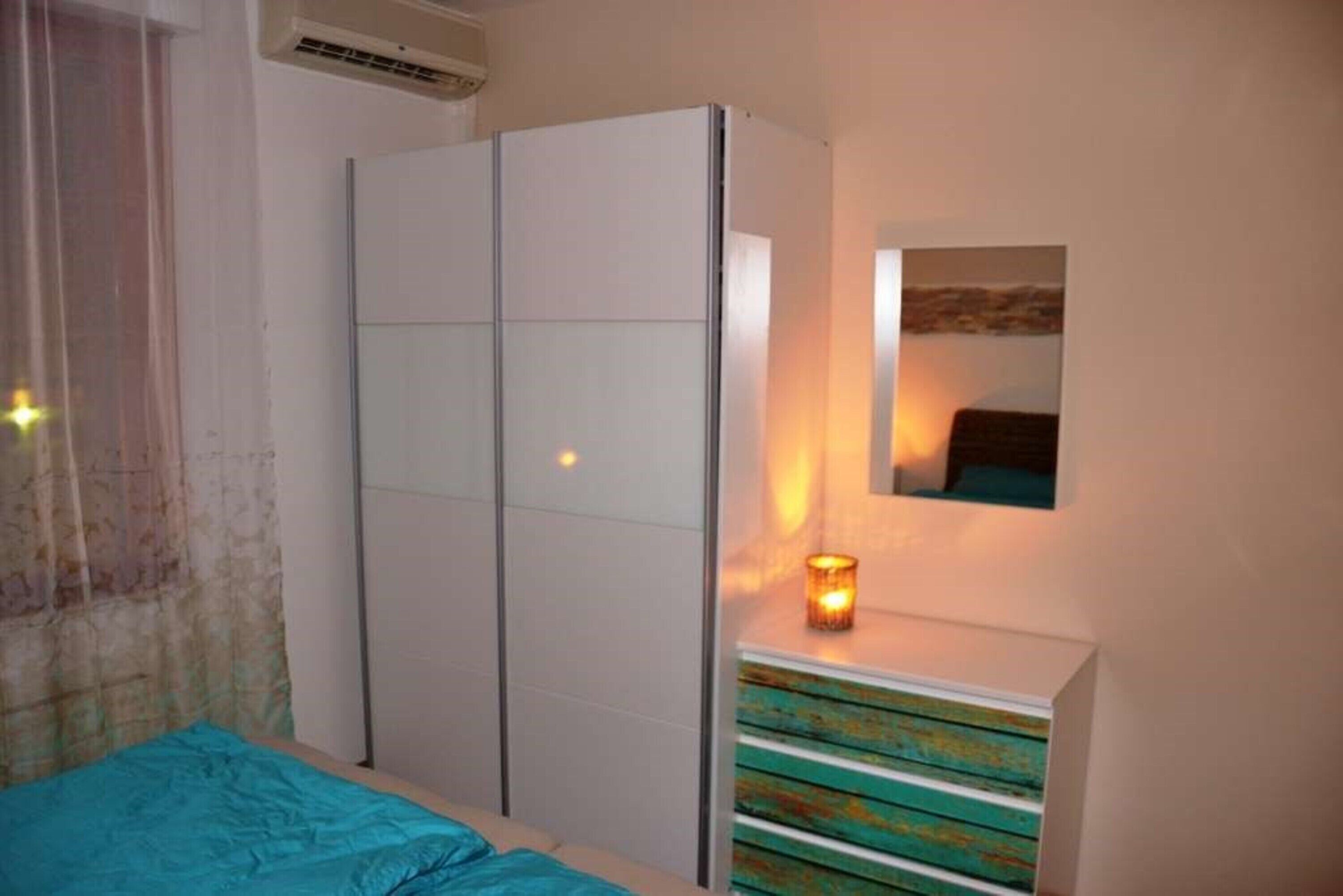 Un dormitorio con cama, armario, cómoda, espejo y una lámpara fijada a la pared.