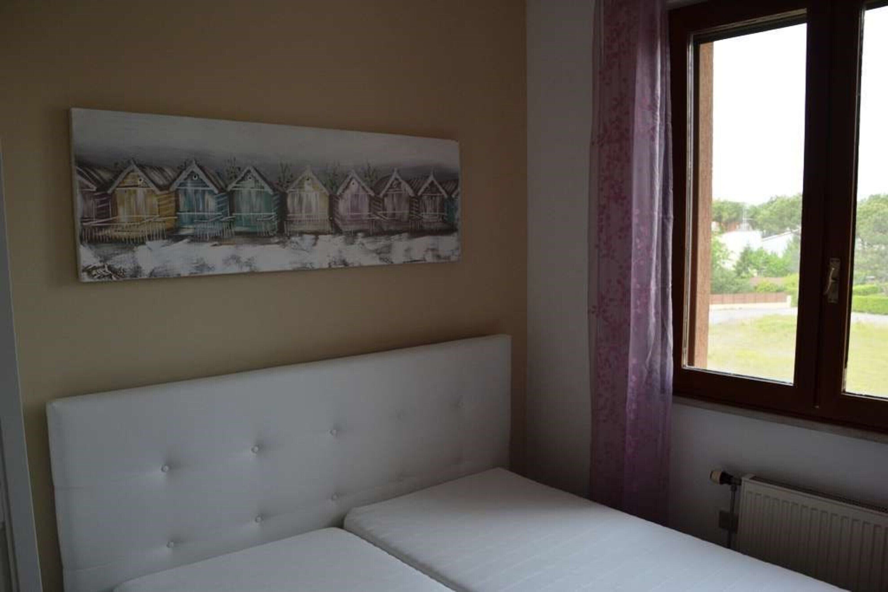 Un dormitorio con una cama individual, una ventana con cortinas y un cuadro de casas en la pared.
