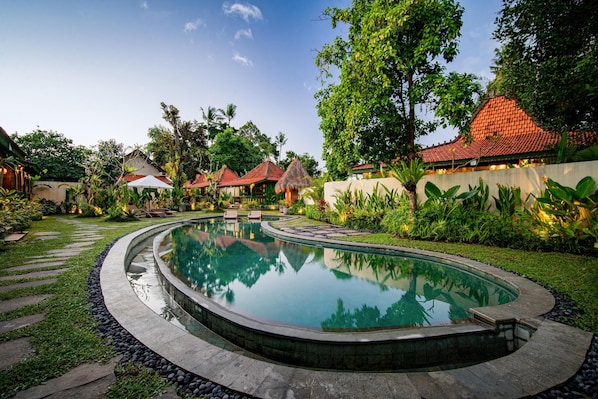 A swimming pool with a curved design, surrounded by a stone walkway and lush greenery. - Juwel Villa Ubud (Ubud)