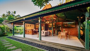 A covered outdoor area with seating and a dining table, surrounded by greenery and a stone pathway. - Juwel Villa Ubud (Ubud)