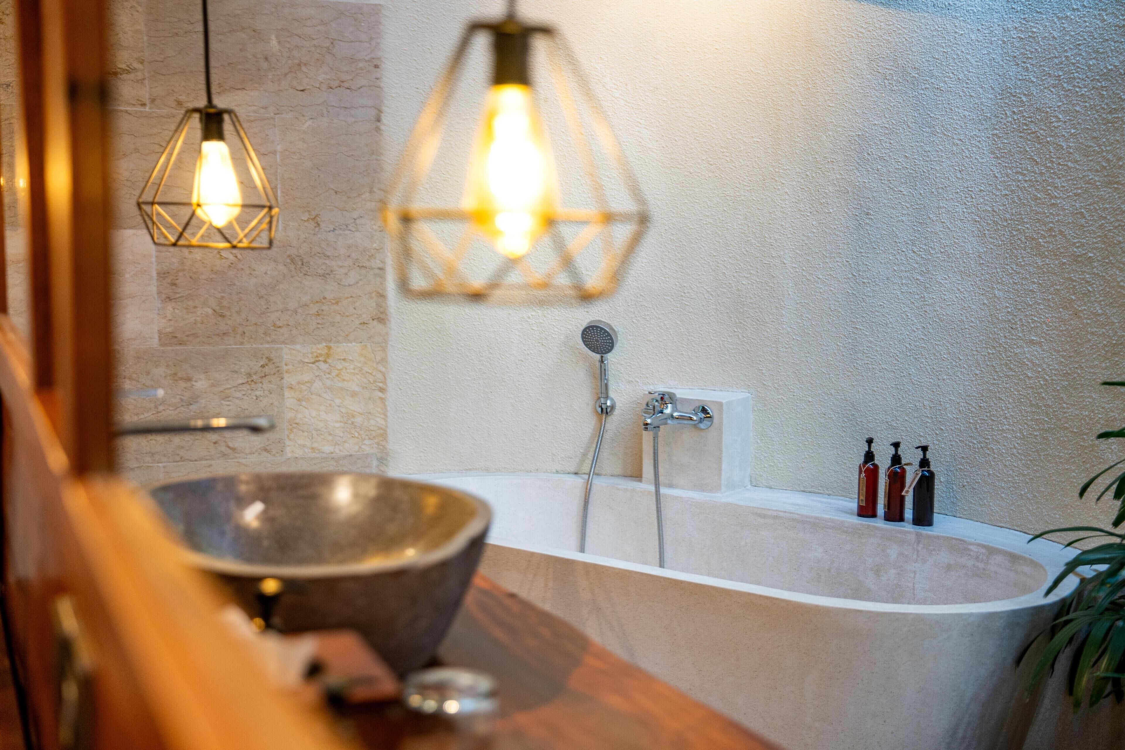A bathroom with a freestanding bathtub, a wooden vanity, a large bowl sink, and two pendant lights.