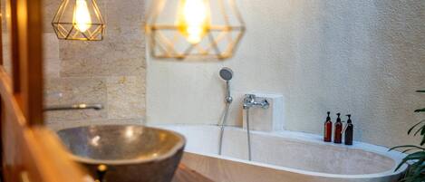 A bathroom with a freestanding bathtub, a wooden vanity, a large bowl sink, and two pendant lights.