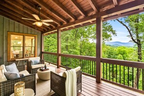 Ein überdachter Außenbereich mit Korbmöbeln, einem Deckenventilator und Blick auf eine bewaldete Landschaft.