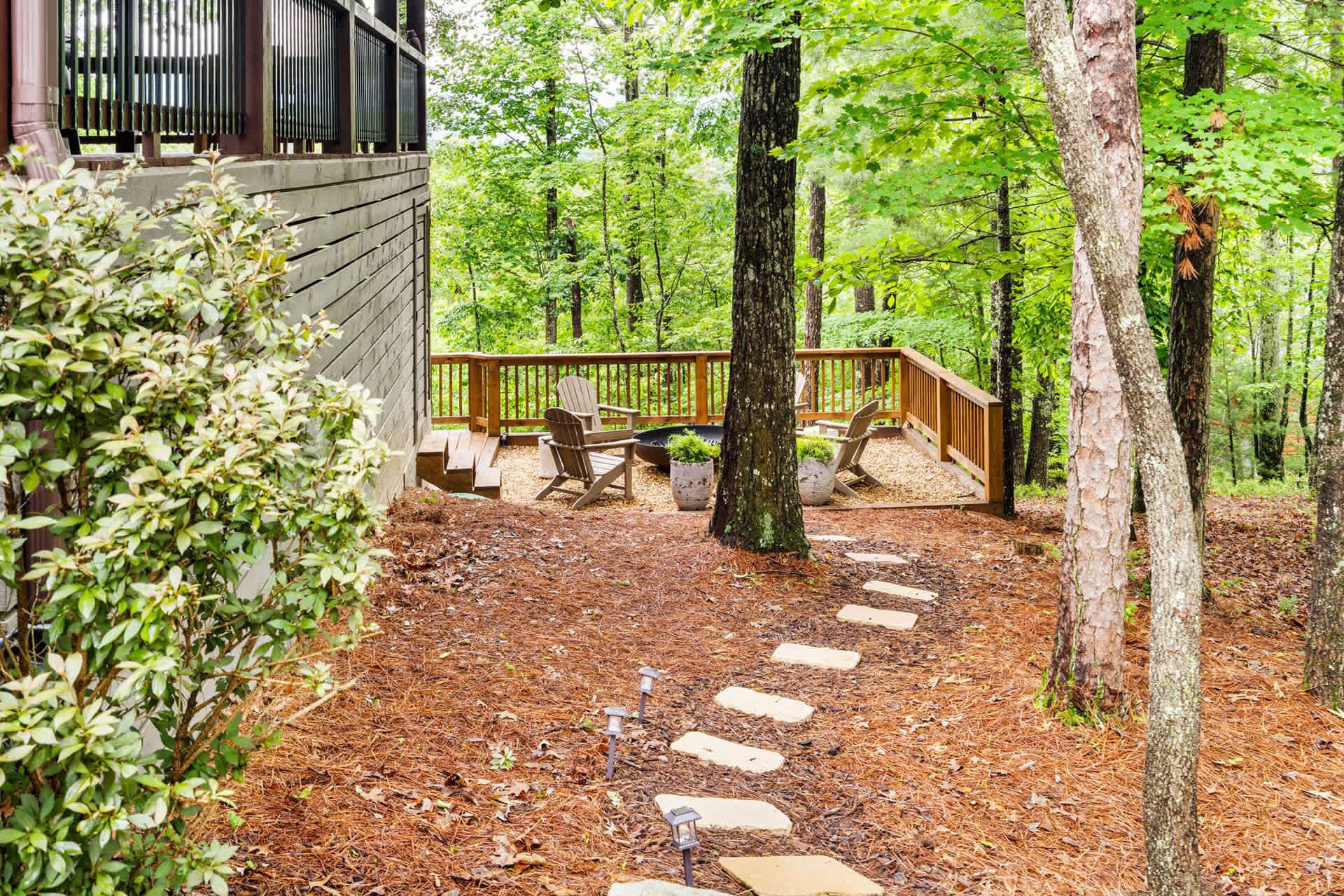 A wooden deck with Adirondack chairs, a stone pathway, and a forested area.