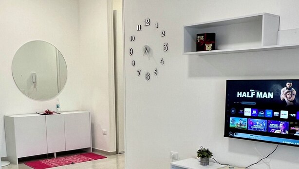A modern living room with a flat-screen TV, a round mirror, a clock, and a minimalist console table. - Your vacation in Otranto a stone's throw from the sea and the historic center (Otranto)