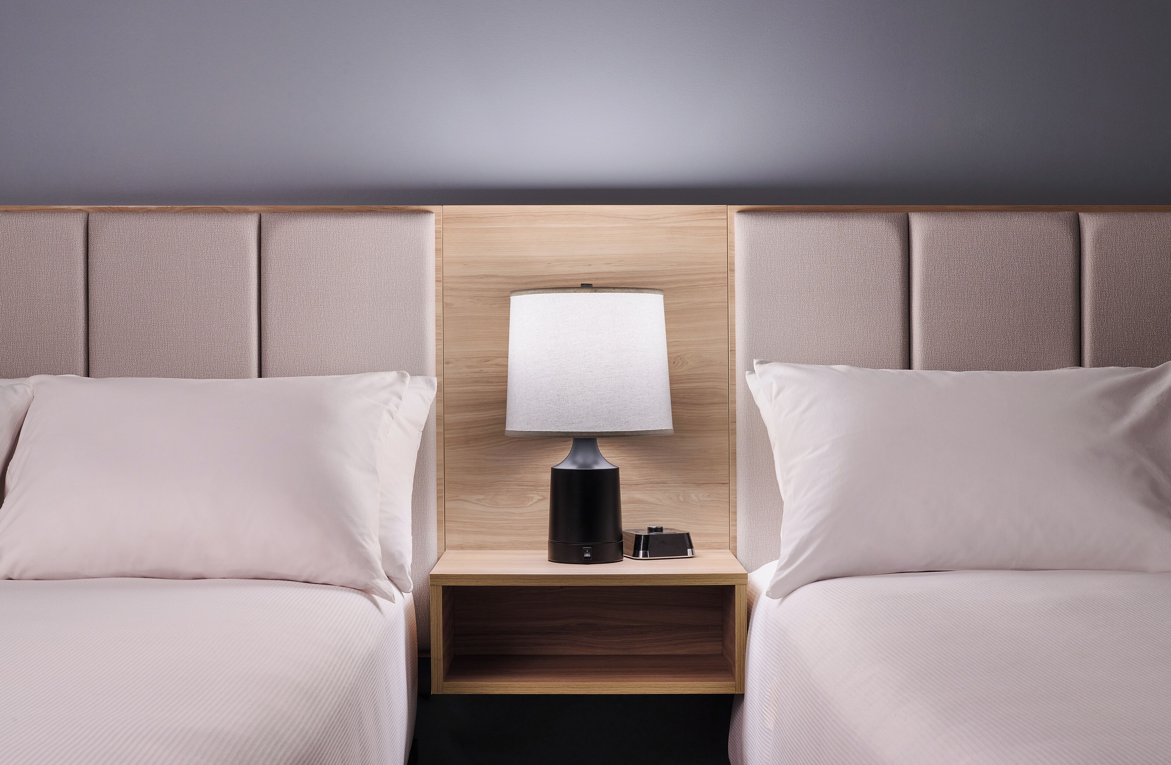 A hotel room with two beds, a nightstand with a lamp, and a wooden headboard.
