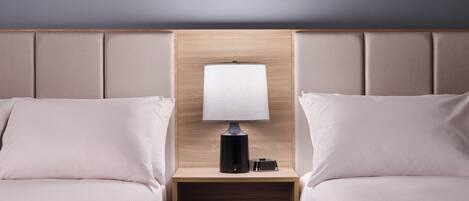 A hotel room with two beds, a nightstand with a lamp, and a wooden headboard.