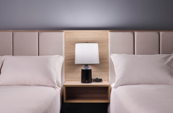 A hotel room with two beds, a nightstand with a lamp, and a wooden headboard.