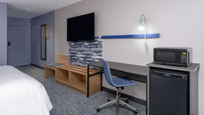 A hotel room with a bed, a desk with a chair, a television, a microwave, and a small refrigerator. - Garner Hotel Pecos by IHG (Pecos)