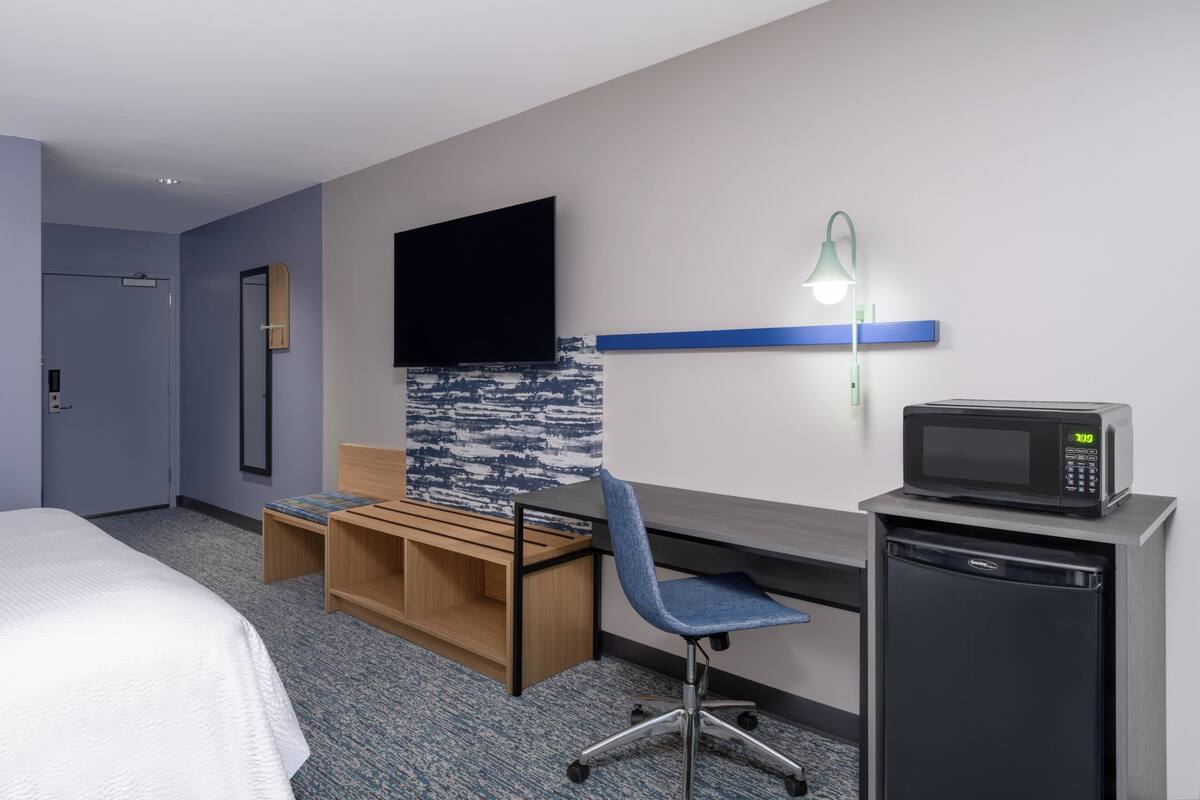 A hotel room with a bed, a desk with a chair, a television, a microwave, and a small refrigerator.