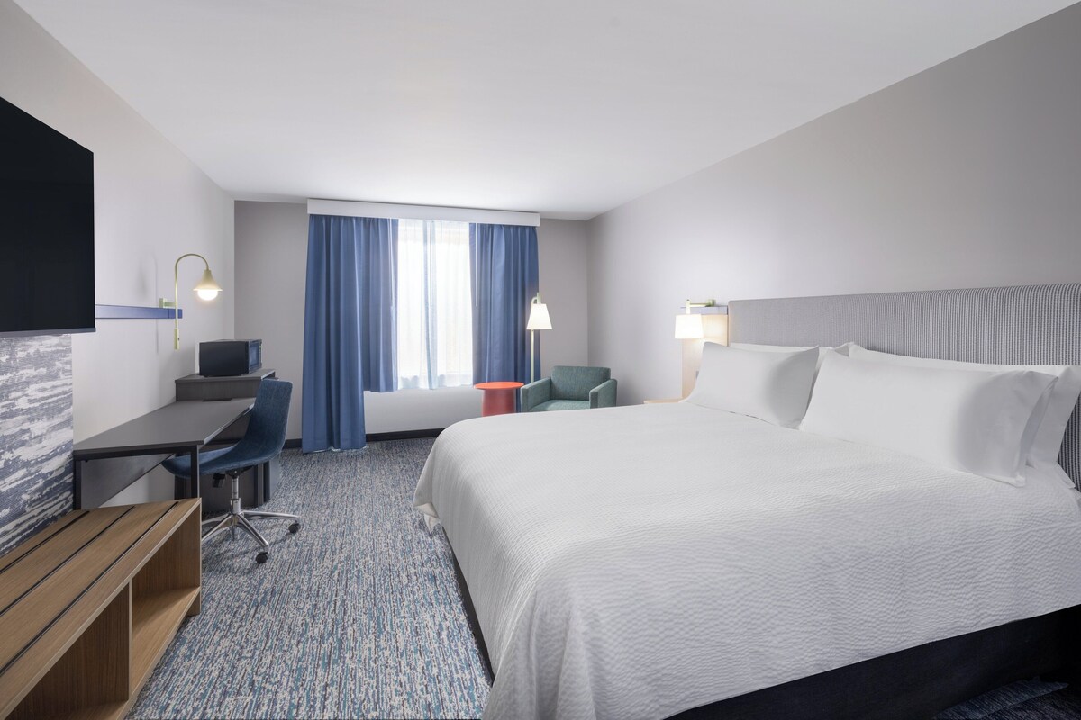 A hotel room with a bed, desk, chair, television, and a window with curtains.