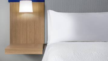 A neatly made bed with a white comforter, a wooden nightstand with a lamp, and a headboard with a blue and white pattern.
