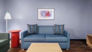A living room with a blue sofa, a red side table, a lamp, and a framed abstract painting on the wall.
