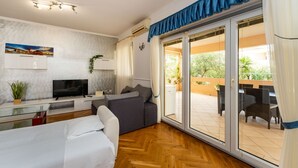 A modern room with a bed, a TV, a sofa, and a sliding glass door leading to an outdoor patio. - Bonvie Apartments in Center B9 (Novalja)