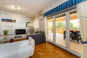 A modern room with a bed, a TV, a sofa, and a sliding glass door leading to an outdoor patio. - Bonvie Apartments in Center B9 (Novalja)