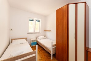 A bedroom with two single beds, a wooden wardrobe, a small bedside table, and a window with blinds. - Bonvie Apartments in Center B9 (Novalja)