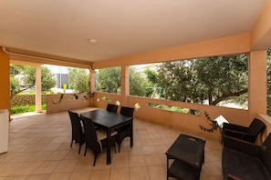 A covered patio with a dining table and chairs, a refrigerator, and a view of greenery. - Bonvie Apartments in Center B9 (Novalja)