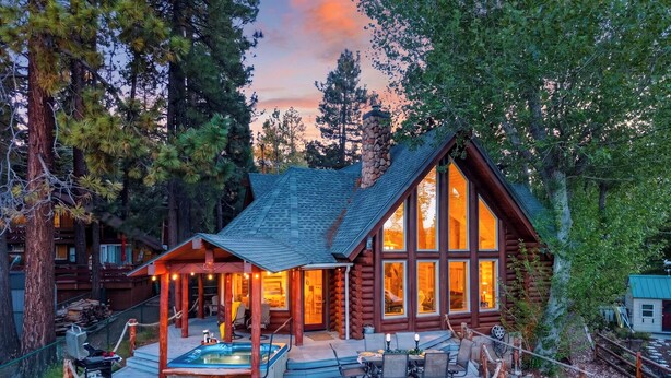 Une cabane en rondins dotée d’une terrasse, d’un bain à remous et d’un espace extérieur aménagé, le tout entouré d’arbres.