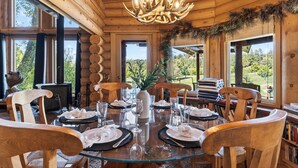 L’intérieur d’un chalet en bois présente une table de salle à manger ronde, préparée pour accueillir six personnes, entourée de chaises en bois.