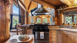 Une cuisine rustique aménagée dans une cabane en rondins, avec un poêle, un four et de grandes fenêtres.