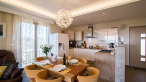 A modern kitchen with white cabinets, a central island, and a dining area with a wooden table and chairs. - Villa Evelyn by Villas Guide (Fažana)