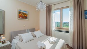 A bedroom with a bed, a nightstand, a painting, a chandelier, and a window with curtains. - Villa Evelyn by Villas Guide (Fažana)