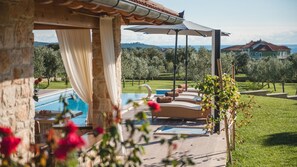 Ein Poolbereich mit Pergola, Sitzgelegenheiten im Freien und Blick auf ein Haus und Bäume.