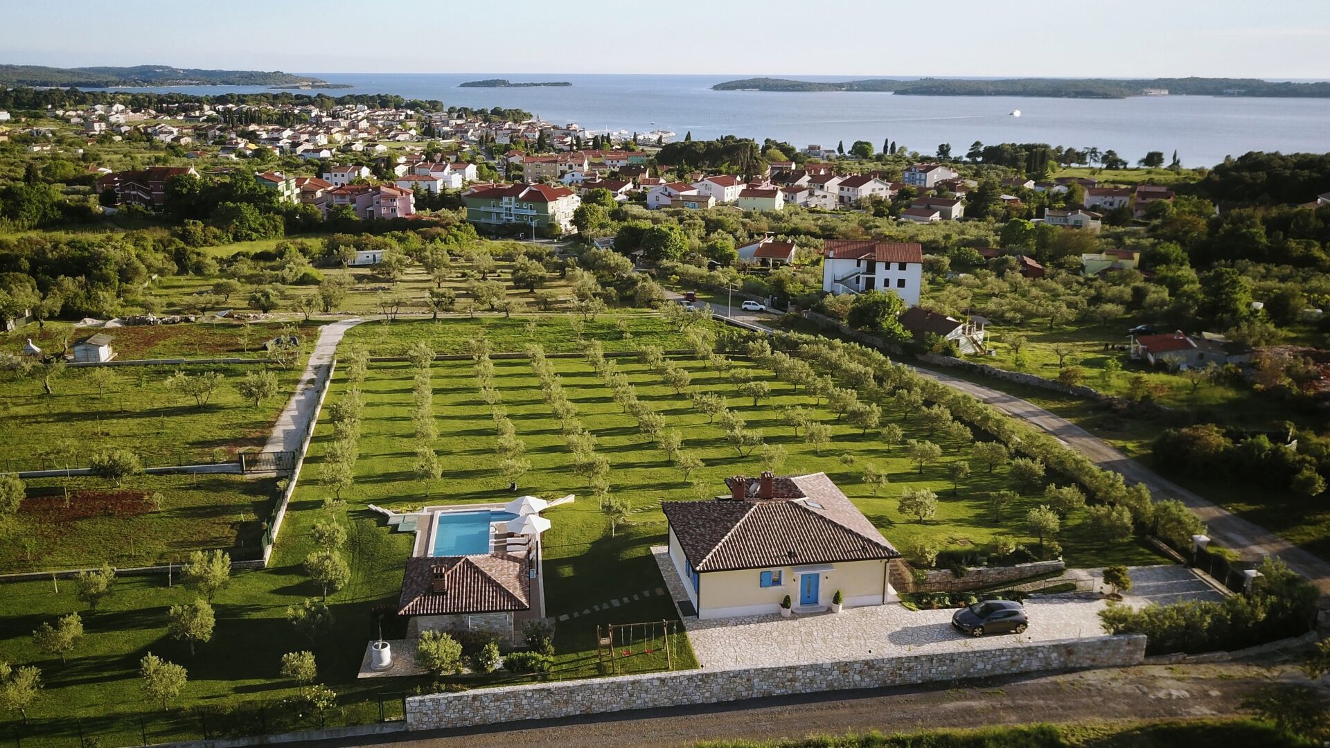 An aerial view of a residential area with houses, a swimming pool, and a large body of water in the background.