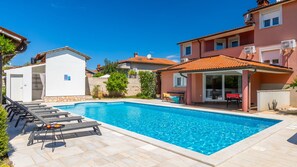 A swimming pool with lounge chairs, a covered patio, and a building with a tiled roof. - Casa Luce by Villas Guide (Pula)