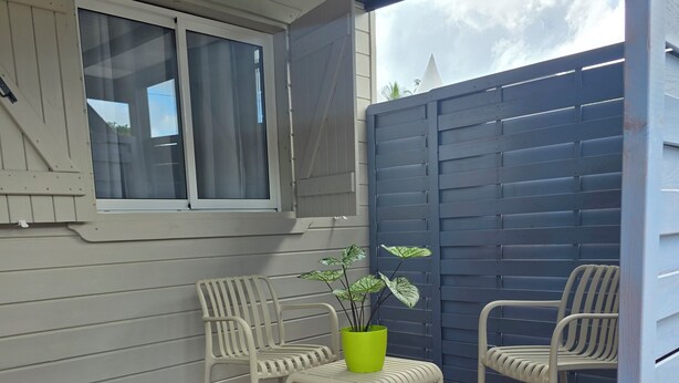 A covered patio with two white chairs, a small table, and a potted plant. - Bungalow Bambou - cozy near CHU, pediatric emergency room and airport (Grande-Terre)