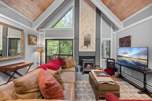 A spacious living room with a fireplace, large windows, and a television.