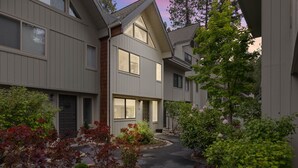 Un edificio residenziale con un ingresso centrale, numerose finestre e un giardino curato con diverse piante e un vialetto.