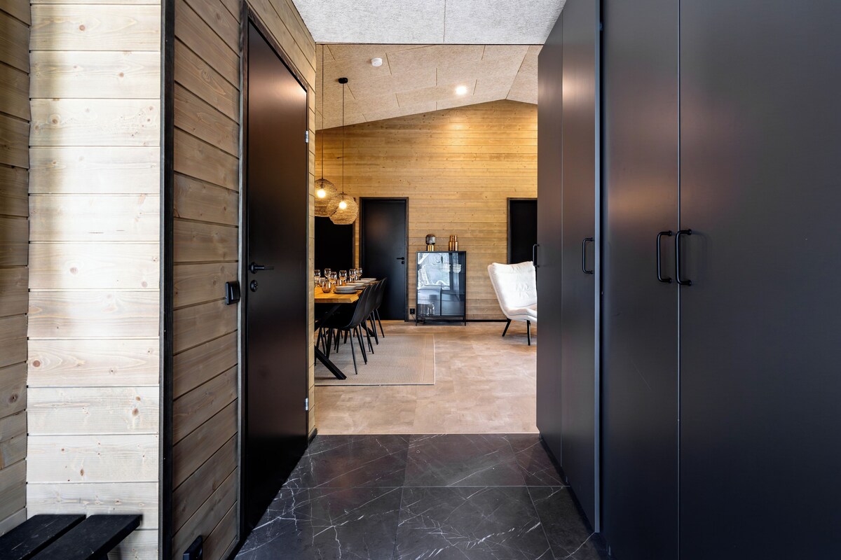 A modern interior with a wooden wall, a dark door, a dining area with a table and chairs, and a black cabinet.