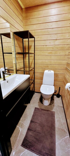 Ein Badezimmer mit Holzvertäfelung, einem weißen Waschbecken, einer Toilette und einem Spiegelschrank.