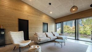 A modern living room with a sofa, chair, and round coffee table, large windows with a view of greenery, and wooden walls. - Villa Noel A  (Lappi)