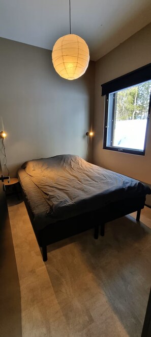 Ein modernes Schlafzimmer mit einem großen Bett, einer Pendelleuchte, einem Fenster mit Aussicht und einem Schreibtisch mit Stuhl.