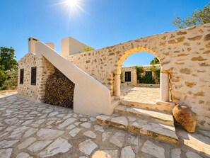 A stone building with a staircase leading to an archway, a tiled courtyard, and a large vase. - Charming Villa with Pool, Sea Views & Traditional Tunisian Architecture (Nabeul Governorate)