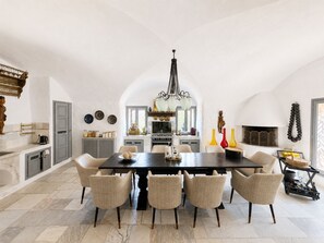 A spacious dining area with a large table and six chairs, a kitchen in the background, and a fireplace with decorative vases. - Charming Villa with Pool, Sea Views & Traditional Tunisian Architecture (Nabeul Governorate)