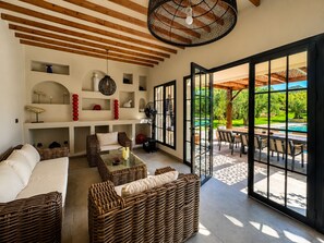 A spacious living area with wicker furniture, a fireplace, and a view of a pool and garden. - Charming Villa with Pool, Sea Views & Traditional Tunisian Architecture (Nabeul Governorate)