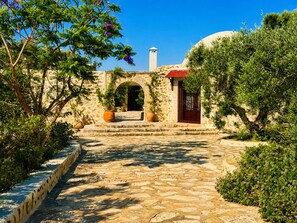 A stone pathway leading to a building with an arched entrance, a red door, and a chimney. - Charming Villa with Pool, Sea Views & Traditional Tunisian Architecture (Nabeul Governorate)