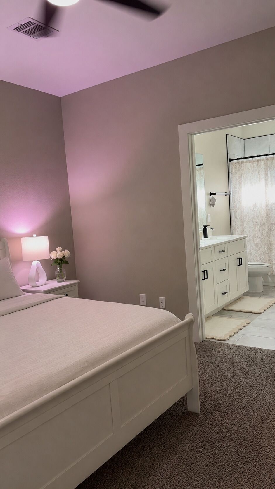A bedroom with a bed, bedside table, lamp, and a nightstand with a vase of flowers.