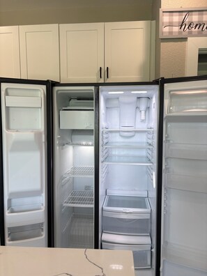 Eine Küche mit einem Zwei-Türen-Kühlschrank, weißen Schränken und einer Marmorarbeitsplatte.