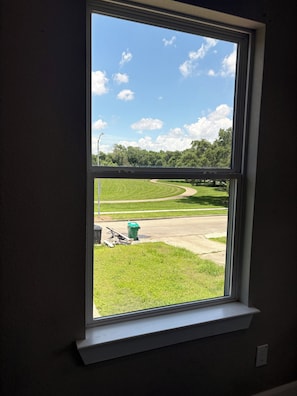 Ein Fenster mit Blick auf eine grüne Rasenfläche, einen gewundenen Weg und einen grünen Mülleimer.
